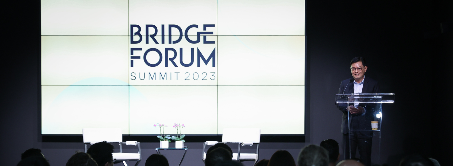 Speaker at podium in front of screen reading "Bridge Forum Summit 2023".